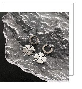 Silver four-leaf clover hoop earrings with radial texture on a black background