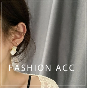 Close-up of geometric gold earrings with small rhinestones and creamy white squares on ear