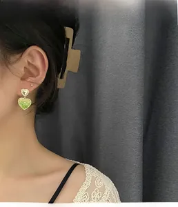 Detail of light green heart-shaped earrings with gold frame on model in profile