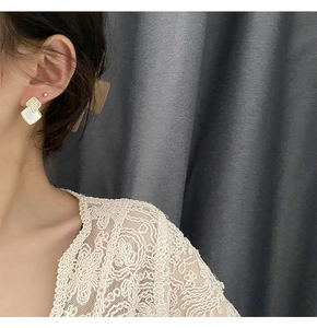 Detailed close-up of square geometric stud earrings with pavé crystals and white mother-of-pearl
