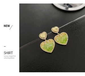 Detail of gold heart earrings featuring green crystals and white zircon accents