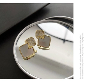 Close-up of geometric gold earrings with white mother-of-pearl and inlaid crystals