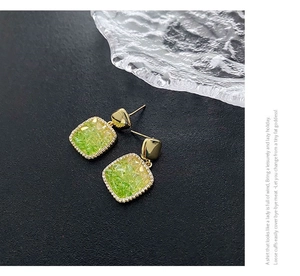 Detail shot of square gold earrings with crushed stones and crystal border on grey surface