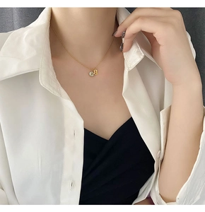 Detail of a gold titanium steel necklace featuring letter A and B charms on a model