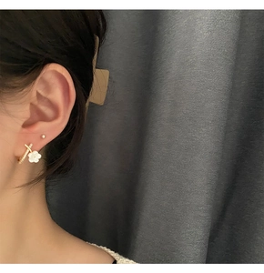 Close-up of elegant X-shaped earrings with micro-inlaid stones and white flower drop