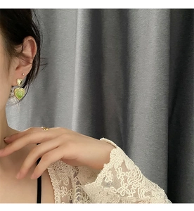 Close-up of green resin heart earrings with gold trim worn on ear with lace detail