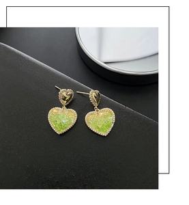 Detailed macro of gold heart earrings with green gradient stones and small crystals