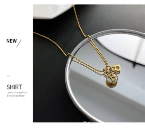 Detail shot of a gold titanium B-letter necklace with pearl disc on mirrored surface
