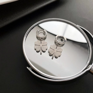 Silver four-leaf clover pendant earrings on a mirror with reflection and metallic texture