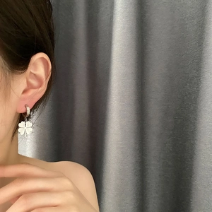 Silver four-leaf clover titanium steel hoop earrings worn on a model with grey background
