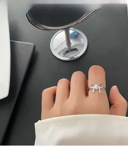 Macro view of minimalist silver hollow bow ring on index finger with elegant metallic finish