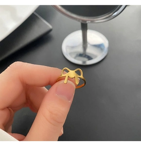 Close-up of gold titanium steel bow ring held between fingers showing delicate cutout detail