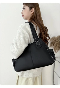 Detail of black pebbled leather tote bag with silver side zipper worn by model