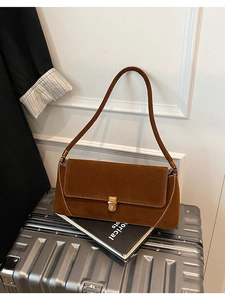 Dettaglio della borsa baguette in camoscio marrone con chiusura dorata e texture fine
