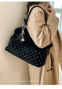 Detail of black tote bag showing star charm, embroidery, and polka dot bottom on trench coat
