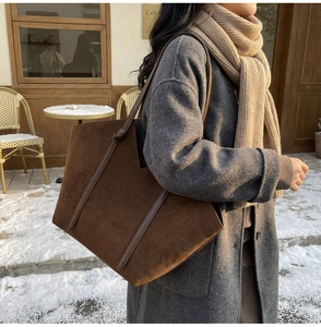 Macro detail of dark brown suede tote bag with leather straps in a snowy winter setting