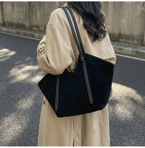 Detail of large black suede tote bag with slim shoulder straps on khaki trench coat