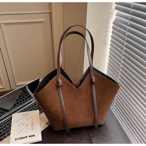 Detail of a brown suede tote bag with a V-shaped cut and knotted strap on a desk