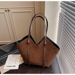 Detail view of brown suede tote bag with V-cut opening and slim straps in minimalist office setting