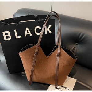 Detail of brown faux suede tote bag with V-cut edge and knot strap on a black sofa