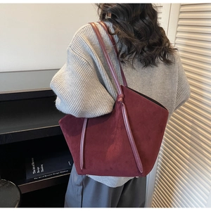 Close-up of burgundy suede tote bag worn by a model in a modern indoor setting