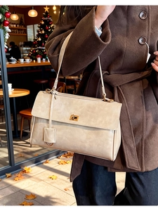Close-up of beige leather shoulder bag with gold metal lock in an autumn cafe setting