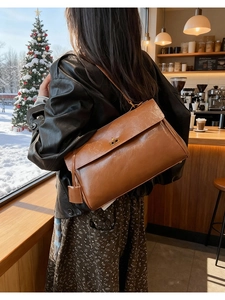 Close-up of caramel leather shoulder bag featuring a golden twist-lock in a cozy cafe