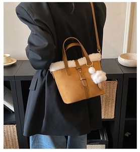 Close-up of brown suede crossbody bag with white faux fur trim and soft pompom charm