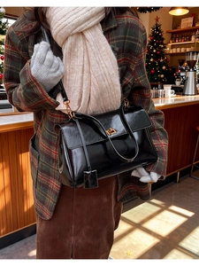 Close-up of black glossy shoulder bag with a gold twist lock on a plaid coat background
