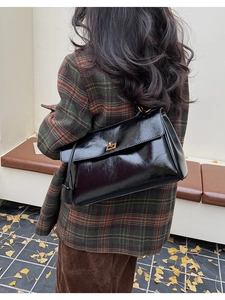 Black glossy shoulder bag with gold clasp shown on a model in an autumn outdoor setting
