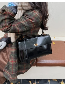 Detail of high-gloss black leather underarm bag with gold metal clasp on autumn background