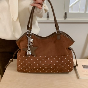 Brown suede tote bag with white polka dots and metal star charms on a wooden table
