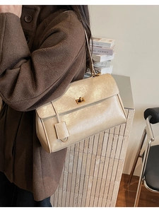 Detail of a beige leather shoulder bag featuring a gold square lock and leather tag