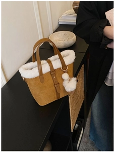 Close-up of brown suede tote bag with white faux fur trim and dual pom-pom keychain detail