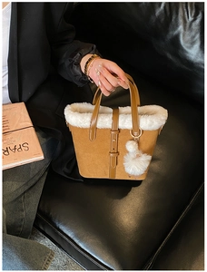 Brown frosted bucket bag with white faux fur trim and pompom detail on leather sofa