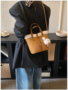 Close-up of brown suede tote bag with white plush trim and heart-shaped pompom charm