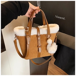 Close-up of brown suede bucket bag with white faux fur trim and fluffy pompom detail