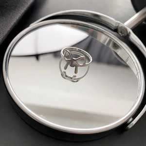 Sleek silver titanium steel bow ring displayed on a circular mirror with reflection