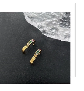 Macro detail of gold-plated hoop earrings with colorful zircon stones on black background