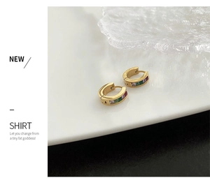 Detail of gold huggie earrings with green and purple square-cut zircons on a white tray