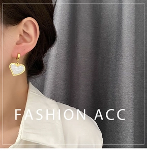 Close-up of heart-shaped gold earring with white shell inlay worn by model