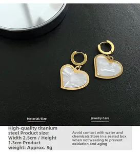 Detailed macro view of gold heart earrings with white marble inlay on a black leather surface