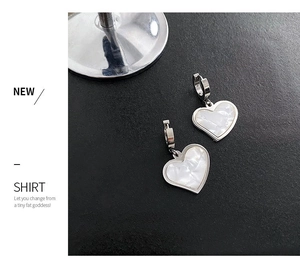 Detail of silver heart hoop earrings with iridescent mother of pearl inlay on black surface