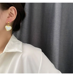 Close-up of heart-shaped gold earrings with white mother-of-pearl inlay on female model