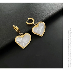 Detail of gold heart earrings with white marble texture and thick hoop closures
