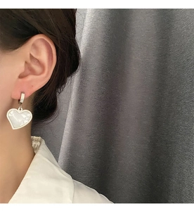 Close-up of heart charm earrings with mother of pearl inlay worn on ear