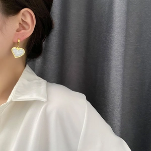 Gold-plated heart hoop earrings with white shell inlay worn by a female model