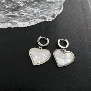 Silver heart hoop earrings with pearl inlay on a dark background in elegant setup