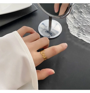 Primo piano di un anello dorato con scritta 'love' traforata indossato da una donna moderna