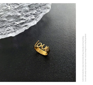 Dettaglio macro di un anello in acciaio dorato con scritta Love traforata ed elegante